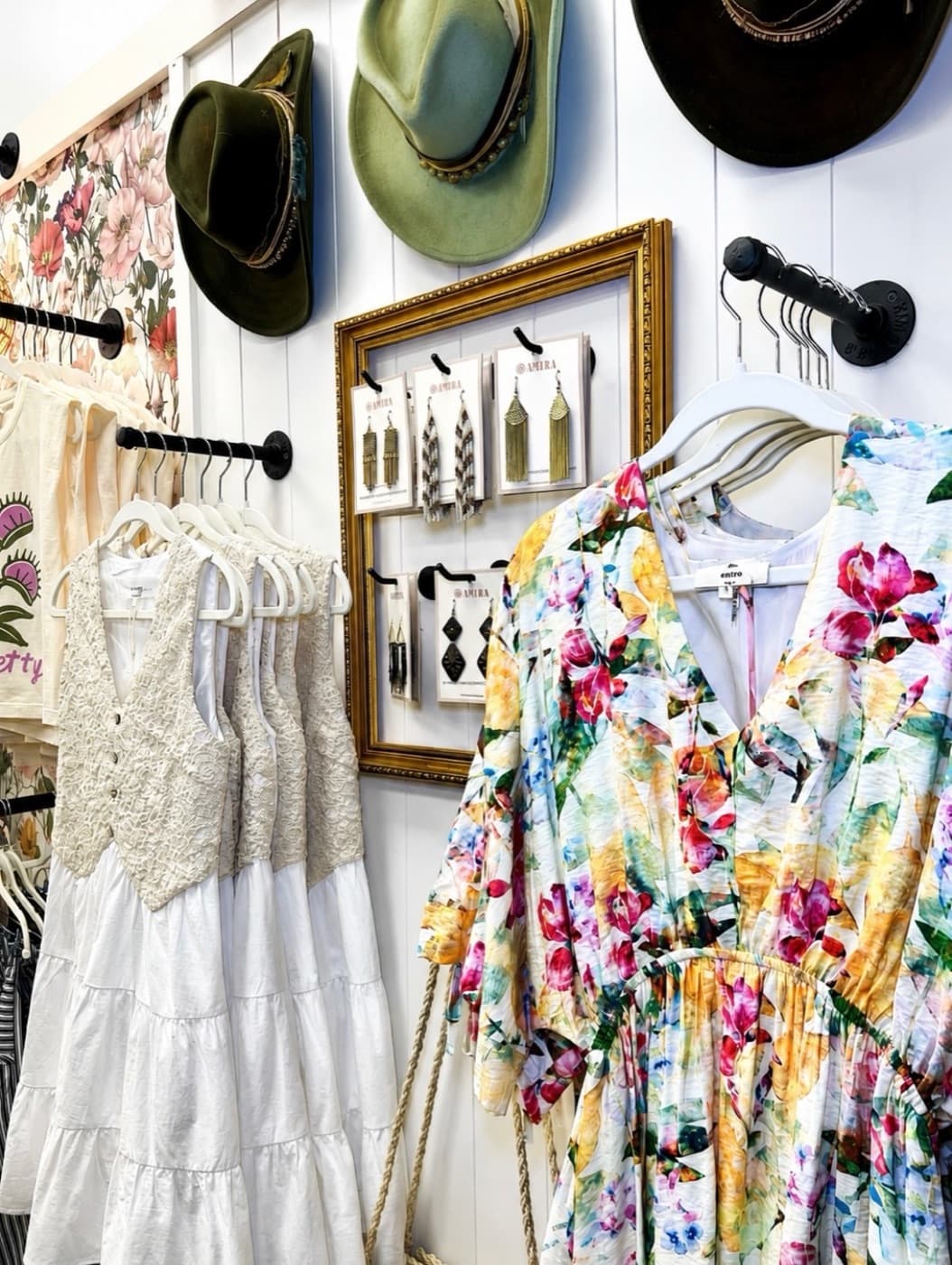 Hats and dresses styled on a boutique wall